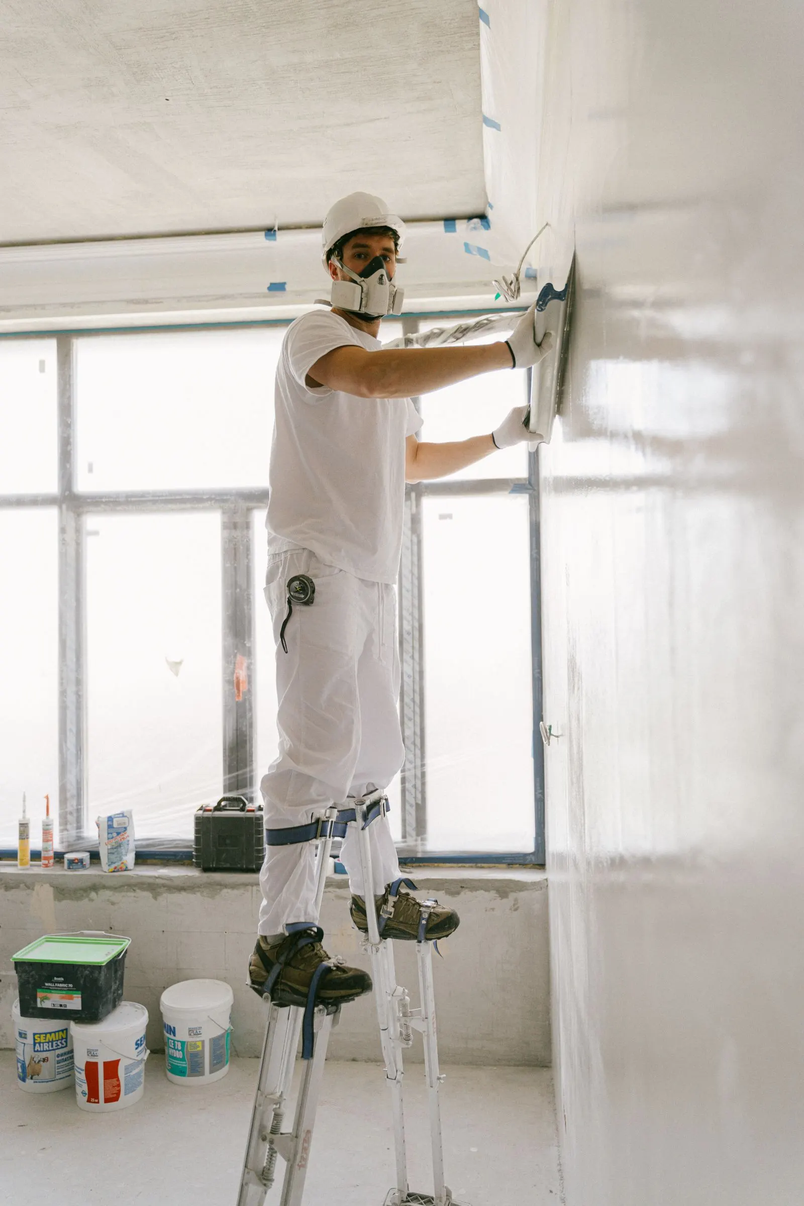 Drywall finisher on stilts skimming a wall